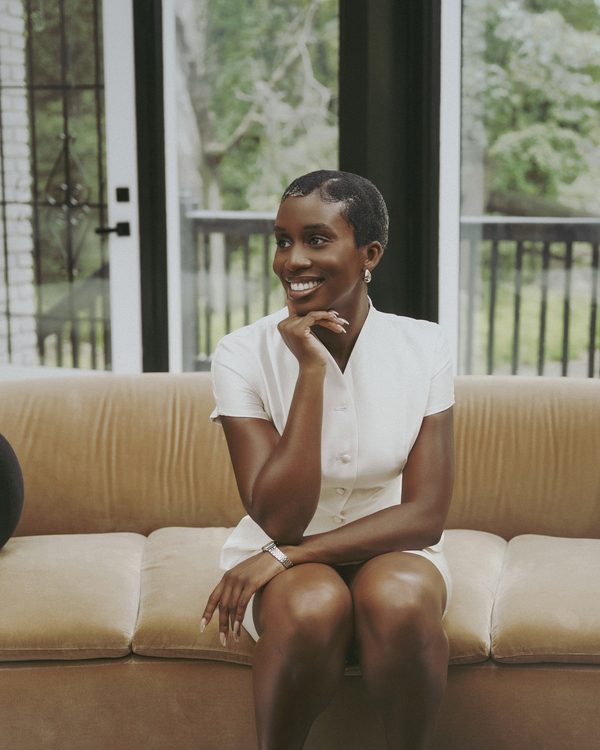 Yvonne Eseonu smiling, seated on a velvet sofa in a sunlit Atlanta living room