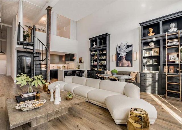 A double-height loft with a black spiral staircase, floor-to-ceiling black library shelving, a rolling ladder and a sculptural white sofa